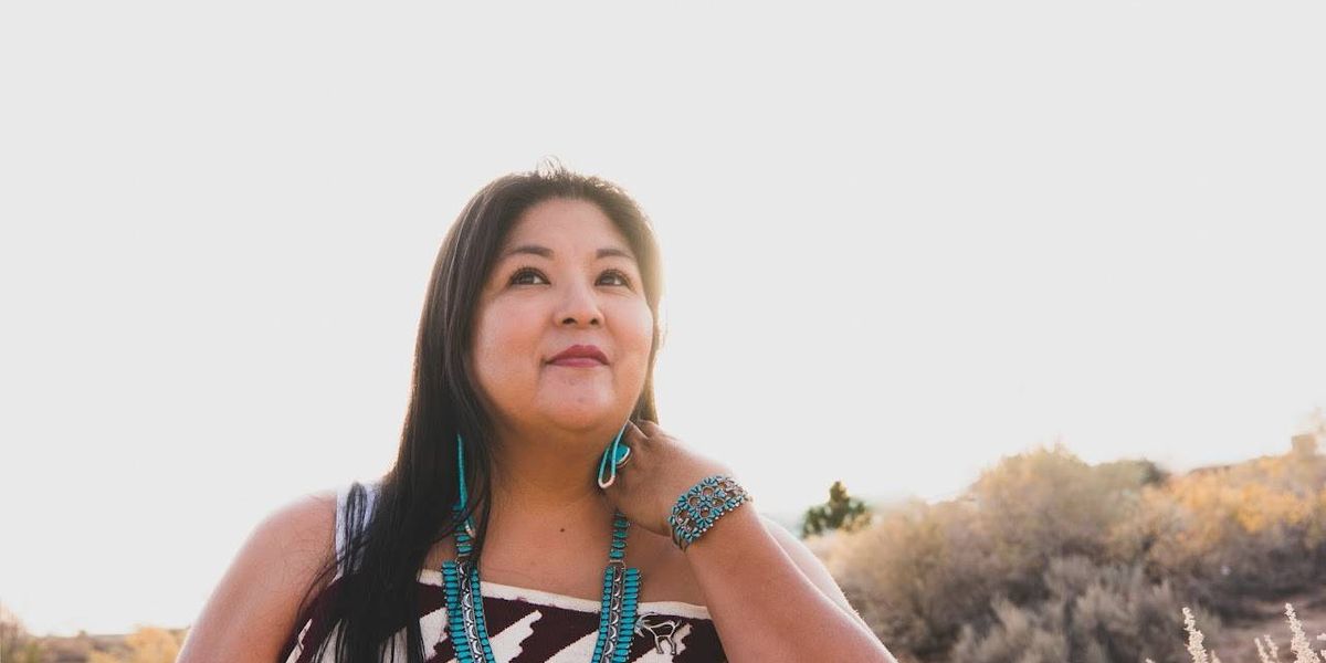 Shayai Lucero, uma mulher nativa americana, em um ambiente florido, refletindo sobre saúde e autocuidado após um ataque cardíaco.